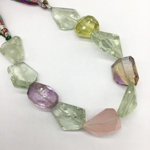 May include: A strand of faceted gemstone beads in shades of green, pink, yellow, and purple. The beads are strung on a cord with a colorful tassel.