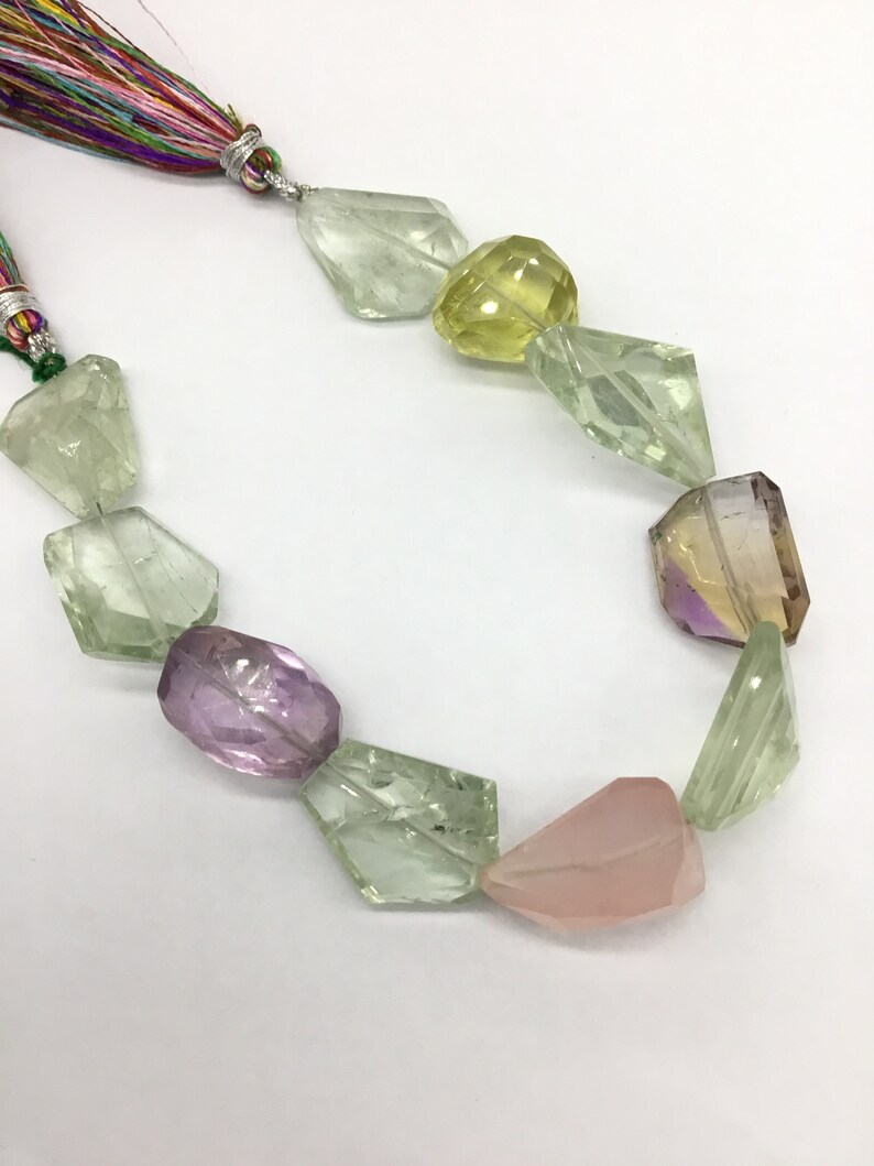 May include: A strand of faceted gemstone beads in shades of green, pink, yellow, and purple. The beads are strung on a cord with a colorful tassel.