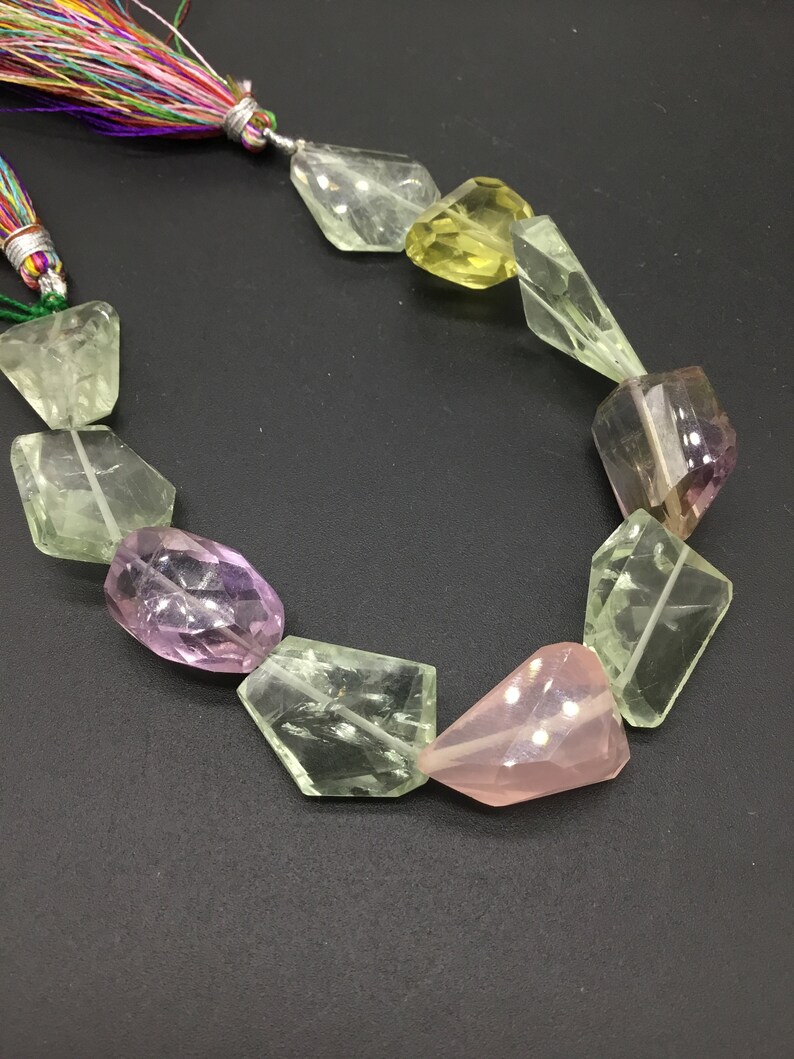 May include: A strand of faceted gemstone beads in shades of green, pink, and purple. The beads are strung on a cord with a colorful tassel.