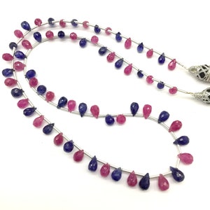 May include: A strand of faceted gemstone beads in a teardrop shape. The beads are alternating colors of pink and blue.