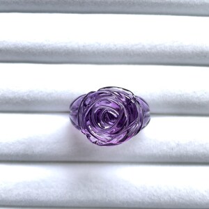Pode incluir: Um anel de rosa de ametista roxo. O anel &eacute; esculpido em uma &uacute;nica pe&ccedil;a de ametista e apresenta um design de rosa detalhado.