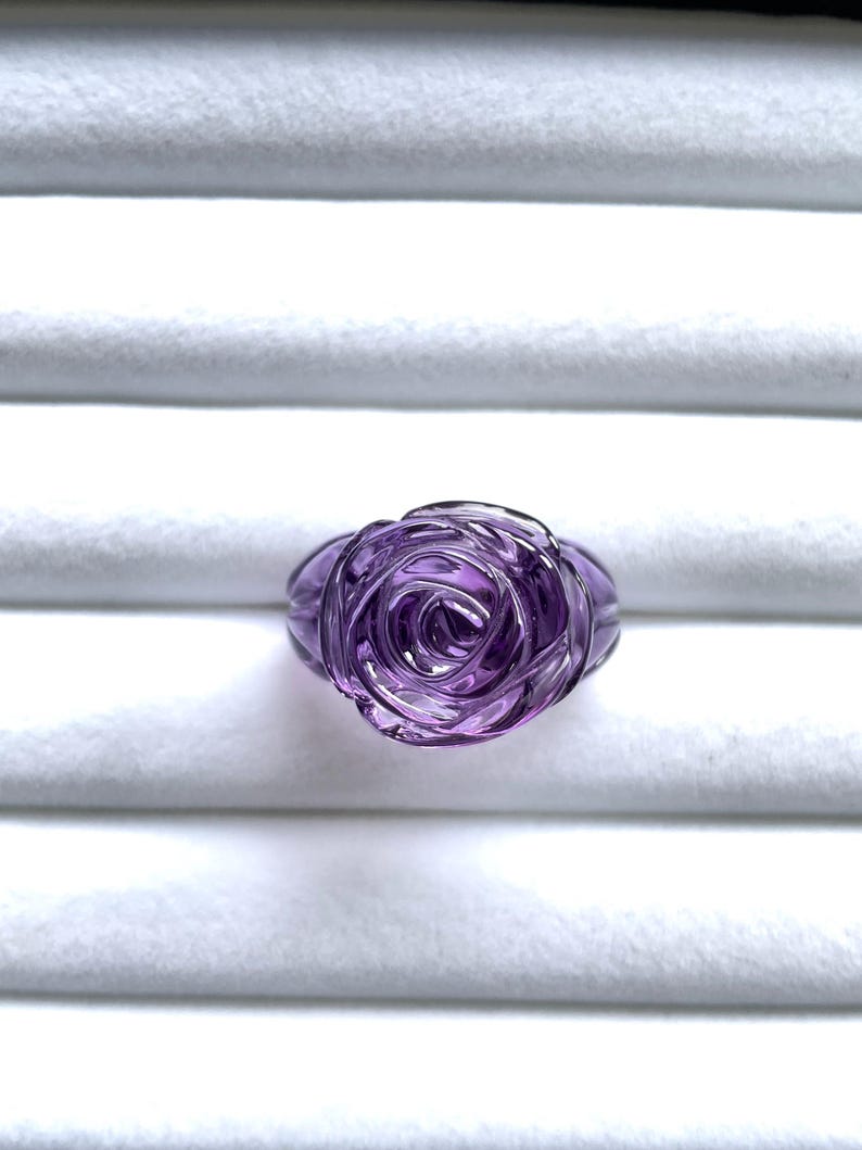 Pode incluir: Um anel de rosa de ametista roxo. O anel &eacute; esculpido em uma &uacute;nica pe&ccedil;a de ametista e apresenta um design de rosa detalhado.