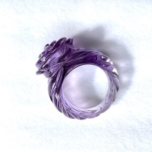 Pode incluir: Um anel de ametista roxo com um design em espiral em forma de rosa. O anel &eacute; esculpido em uma &uacute;nica pe&ccedil;a de ametista e tem um acabamento liso e polido.