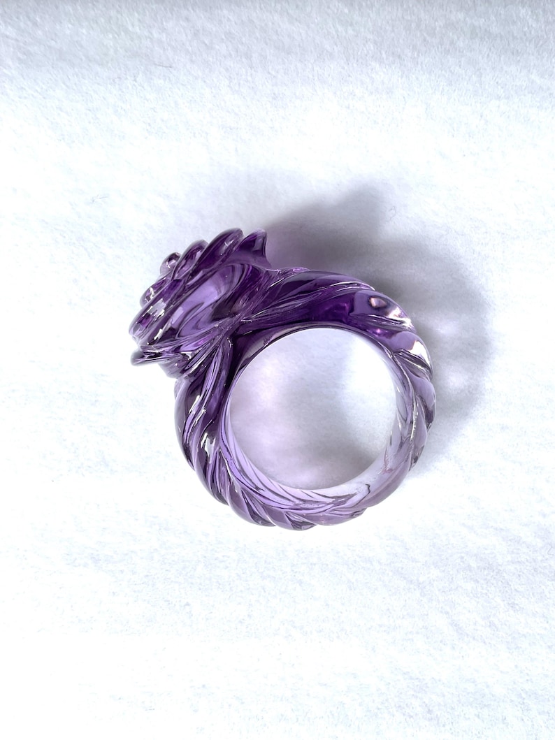 Pode incluir: Um anel de ametista roxo com um design em espiral em forma de rosa. O anel &eacute; esculpido em uma &uacute;nica pe&ccedil;a de ametista e tem um acabamento liso e polido.