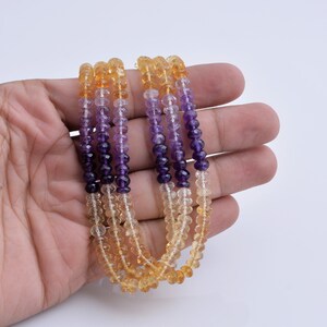 May include: A multi-strand necklace made of faceted gemstone beads. The beads are a gradient of colors, starting with a light yellow, then transitioning to a light orange, and finally to a deep purple.