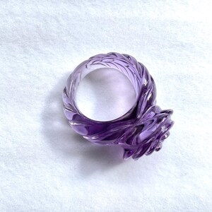 Pode incluir: Um anel de ametista roxo com um design de rosa. O anel &eacute; esculpido em uma &uacute;nica pe&ccedil;a de ametista e tem uma banda torcida.