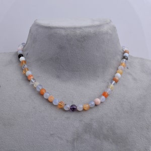 May include: A multi-colored gemstone necklace with round beads in shades of blue, orange, pink, and purple. The necklace is displayed on a gray mannequin.