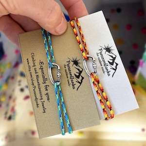 Peut inclure: Deux bracelets en paracorde avec un charme de mousqueton argenté. Les bracelets sont bleu et vert, et orange et jaune. La carte indique "Paracord Janka - pour les âmes d'extérieur".