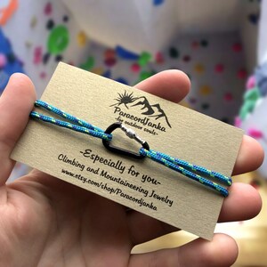 Pu&ograve; includere: Un braccialetto in paracord blu e verde con un moschettone argentato. Il braccialetto &egrave; su una carta marrone con il testo "ParacordJanka - for outdoor souls - Especially for you - Climbing and Mountaineering Jewelry www.etsy.com/shop/ParacordJanka"