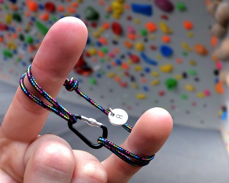 Pu&ograve; includere: Un braccialetto in corda nero e multicolore con un ciondolo argentato e un moschettone nero.