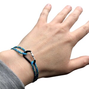 Pu&ograve; includere: Un braccialetto in corda blu e verde con un moschettone nero.
