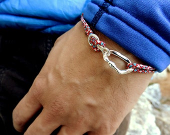 May include: A red, white, and blue braided rope bracelet with a silver carabiner clasp.