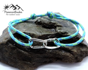 May include: A turquoise, green, and purple paracord bracelet with a silver carabiner clasp. The clasp is engraved with "925".