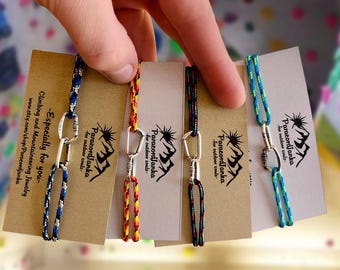 May include: Four colorful paracord bracelets with silver carabiners. Each bracelet has a card with the text "Paracord Janka - for outdoor souls".