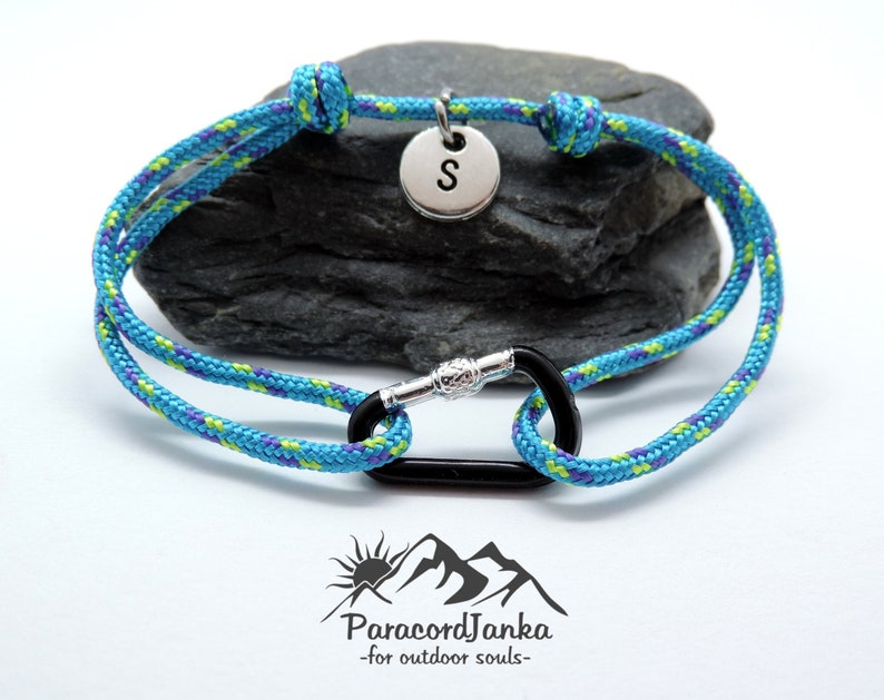 Pu&ograve; includere: Un braccialetto in paracord blu e verde con un moschettone nero e un ciondolo argentato con la lettera "S".