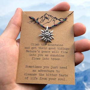 May include: A brown card with a quote about climbing mountains and finding peace in nature. The card has a silver mountain charm attached to a colorful cord.