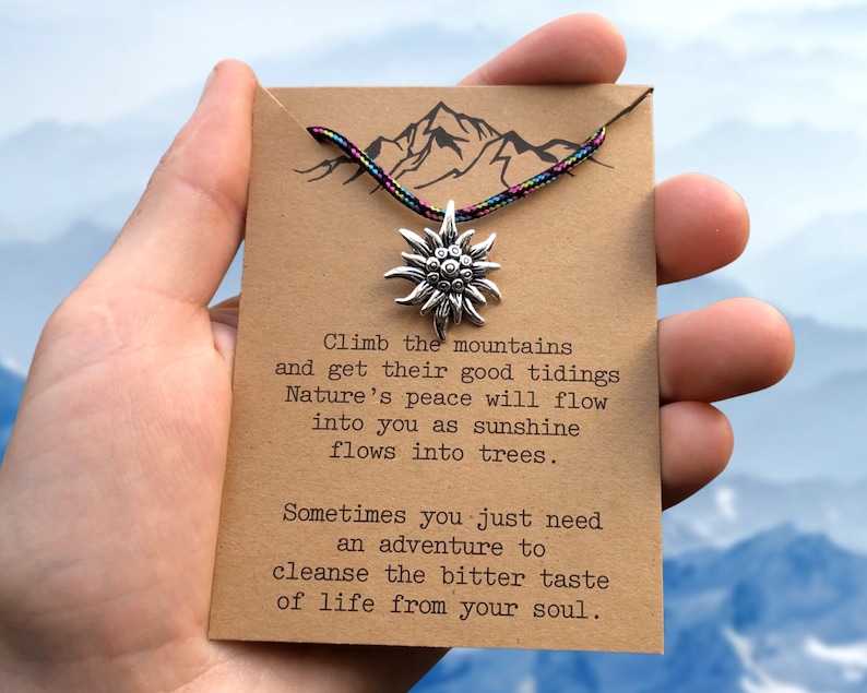 May include: A brown card with a quote about climbing mountains and finding peace in nature. The card has a silver mountain charm attached to a colorful cord.