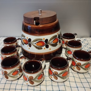 Op de afbeelding: Een vintage keramische punchkom met een houten deksel en acht bijpassende bekers. De kom en de bekers zijn versierd met een bruin, oranje en groen bloemenpatroon.
