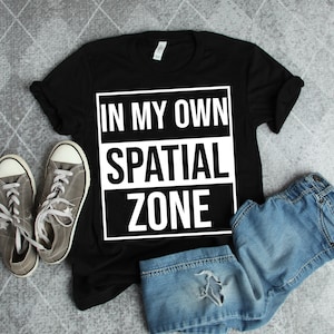 Op de afbeelding: Zwart T-shirt met witte tekst die "In My Own Spatial Zone" zegt.