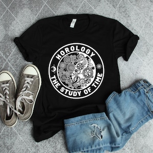 Puede incluir: Camiseta negra con un gráfico circular blanco que dice "Horology The Study of Time" con un diseño de engranajes y una luna creciente dentro del círculo.