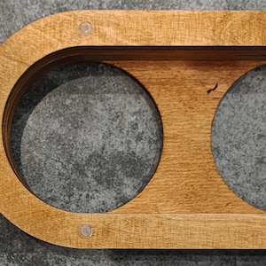 May include: A wooden coaster with two circular cutouts for holding mugs or glasses. The coaster has a natural wood finish and is decorated with two small silver dots.