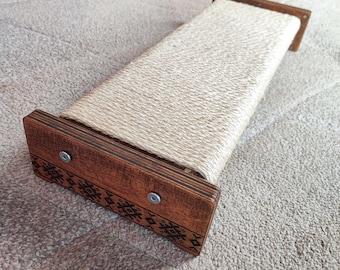 May include: A rectangular cat scratching post with a woven sisal scratching surface. The post has dark brown wooden end pieces with decorative etched patterns and is secured with metal screws. A pet accessory.