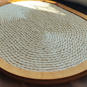 May include: A round, natural fiber woven mat with a wood frame. The mat is beige and has a circular pattern.