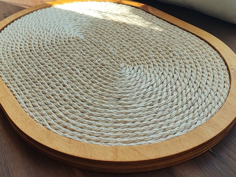 May include: A round, natural fiber woven mat with a wood frame. The mat is beige and has a circular pattern.