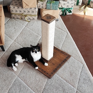 May include: A black and white cat is lying on a wooden cat scratching post with a sisal rope covered post. The post has a square base with a decorative carved design.