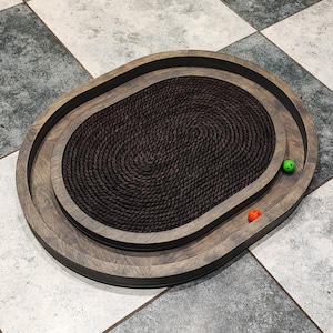 May include: A brown wooden oval cat scratching post with a rope-covered center. Two small green and orange balls are on the surface of the scratching post.