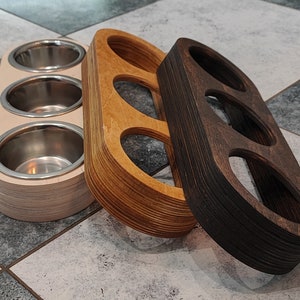 May include: Three wooden bowls with different finishes. The bowl on the left is white with three round indentations. The middle bowl is light brown with two round indentations. The bowl on the right is dark brown with three round indentations.