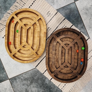 Könnte beinhalten: Zwei ovale Holz-Labyrinthspiele mit unterschiedlichen Holztönen. Ein Labyrinth ist hellbraun mit grünen und roten Murmeln. Das andere Labyrinth ist dunkelbraun mit orangefarbenen und blauen Murmeln.