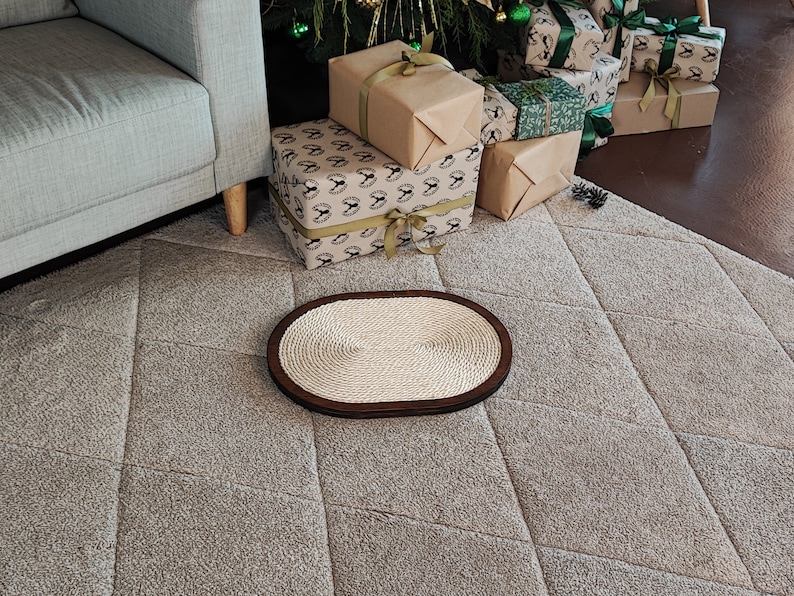 May include: A light brown oval-shaped cat scratching post with a woven rope surface. The scratching post is on a light gray carpet with a diamond pattern.