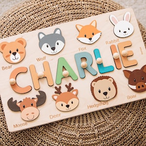 Könnte beinhalten: Holzpuzzle mit dem Namen "CHARLIE" in bunten Buchstaben. Das Puzzle enthält tierförmige Teile wie einen Bären, Wolf, Fuchs, Kaninchen, Elch, Hirsch, Igel und Wildschwein. Das Puzzle liegt auf einer gewebten Oberfläche.