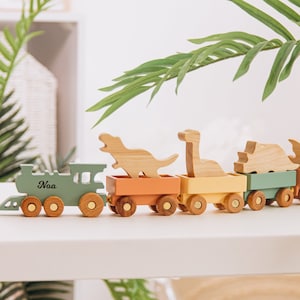 May include: A wooden toy train with a green engine and colourful cars. The engine has the name "Noa" written on it. The cars are decorated with dinosaur shapes.