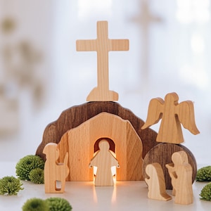 Può includere: Scena della natività in legno con una croce, un angelo e figure in piedi intorno a una tomba. La tomba è illuminata dall'interno e le figure sono in legno chiaro.