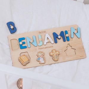 May include: Wooden name puzzle spelling "BENJAMIN" in blue and white letters, with the word "BLESS" above and "Forevermore" below. Includes a separate blue "B" and wooden cutouts of a book, angel, cross, and church.