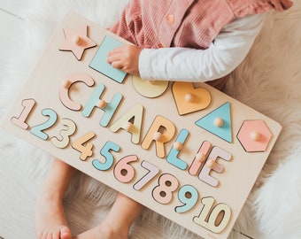May include: A wooden puzzle board with pastel colored letters spelling out the name "Charlie" and numbers 1 through 10. The puzzle pieces are shaped like geometric shapes, including a star, heart, and hexagon. A child is playing with the puzzle.