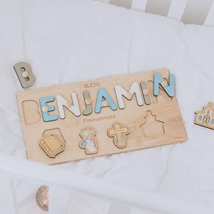 May include: Wooden name puzzle with the name "BENJAMIN" in blue, gray, and white letters. The puzzle includes the word "BLESS" and "Forevermore". Additional wooden shapes include a book, angel, cross, house, and the letter "B".