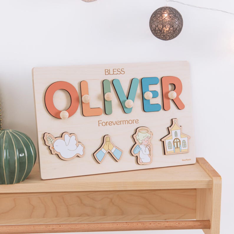 May include: Wooden puzzle with the name "OLIVER" in orange, green, and blue letters. The word "BLESS" is above the name, and "Forevermore" is below. Includes dove, praying hands, angel, and church-shaped puzzle pieces.
