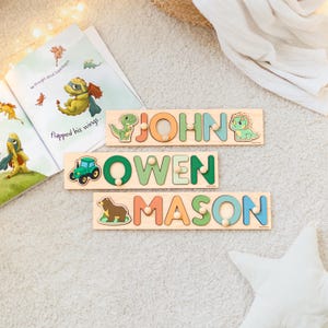 May include: Three wooden name puzzles with the names "JOHN", "OWEN", and "MASON" in colorful letters. Each puzzle features a different animal or vehicle: a dinosaur, a tractor, and a bear. A children's book is open in the background.