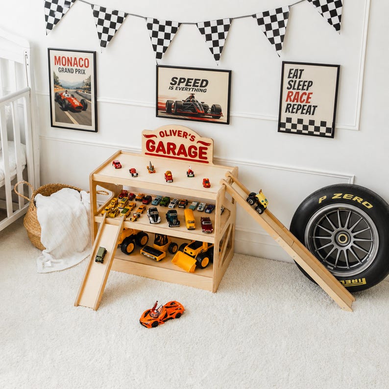 May include: A light-colored wooden toy garage with two levels, a top sign reading OLIVER'S GARAGE, and two attached ramps. The garage is filled with various small toy cars and construction vehicles, with an orange sports car on the floor in front.