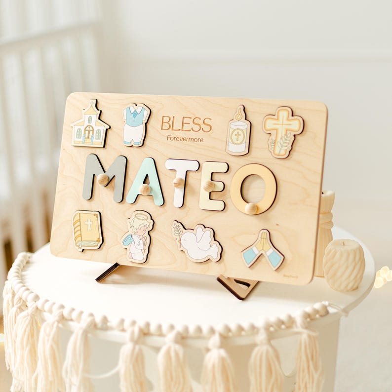 May include: Wooden puzzle board with the name "MATEO" in colorful letters. The board includes religious-themed puzzle pieces like a church, cross, and angel. The word "BLESS Forevermore" is printed above the name.