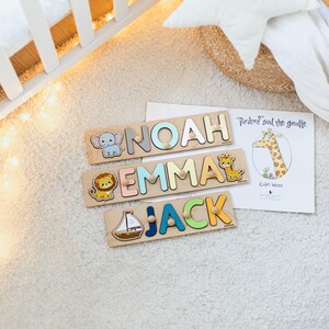 Pode incluir: Quebra-cabe&ccedil;as de madeira com os nomes "Noah", "Emma" e "Jack" em letras coloridas. Cada quebra-cabe&ccedil;a inclui uma ilustra&ccedil;&atilde;o de animal: um elefante, um le&atilde;o e uma girafa. Um livro infantil com uma girafa tamb&eacute;m &eacute; vis&iacute;vel.