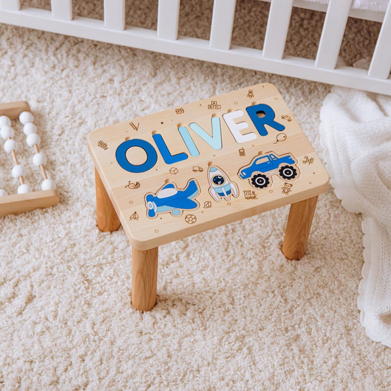 Personalized wooden name stool “Oliver” with transport theme featuring airplane, rocket, and monster truck. Montessori-inspired toddler furniture designed for both play and everyday use — perfect as a step stool, seat, or learning toy. Removable letters help develop fine motor skills, coordination, and early name recognition. Crafted from solid natural wood with smooth edges and child-safe finishes. A meaningful gift for first birthday, baby boy, or modern nursery decor.