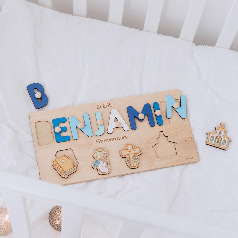 May include: Wooden name puzzle spelling "BENJAMIN" in blue and white letters, with the word "BLESS" above and "Forevermore" below. Includes a separate blue "B" and wooden cutouts of a book, angel, cross, and church.