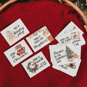 May include: A set of 10 Christmas activity cards with watercolor illustrations. The cards feature activities like seeing a holiday play, drinking hot chocolate, making a treat for neighbors, hanging a wreath, having a picnic by the Christmas tree, and making a family Christmas cards.