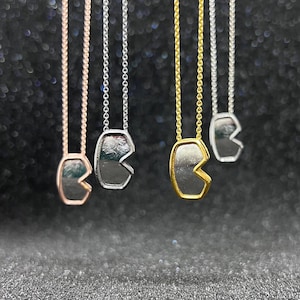 May include: Four necklaces with different coloured chains and a pendant shaped like a Pac-Man character. The pendants are silver, gold, rose gold, and silver.