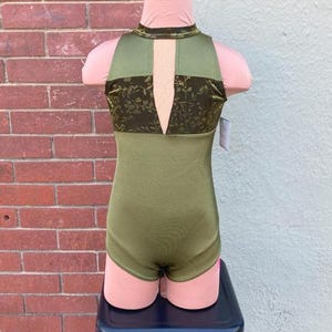 May include: A sleeveless leotard with a high neckline and a keyhole opening at the back. The leotard is made from a green fabric with a floral pattern and a solid green bottom.