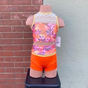 May include: Orange and yellow floral print dance leotard with a white lace neckline and matching orange shorts. The leotard and shorts are on a mannequin.